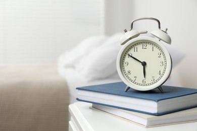 Photo of Alarm clock and books on white nightstand in bedroom, space for text