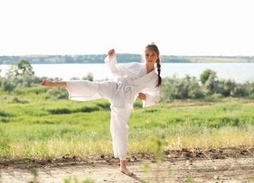 Photo of Cute little girl in kimono practicing karate outdoors