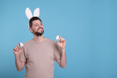 Happy man in bunny ears headband holding painted Easter eggs on turquoise background. Space for text