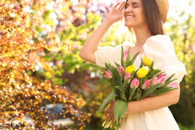 Photo of Beautiful young woman with bouquet of tulips in park, focus on flowers. Space for text