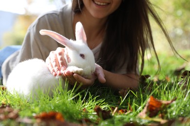 Photo of Happy woman with cute white rabbit on grass, closeup