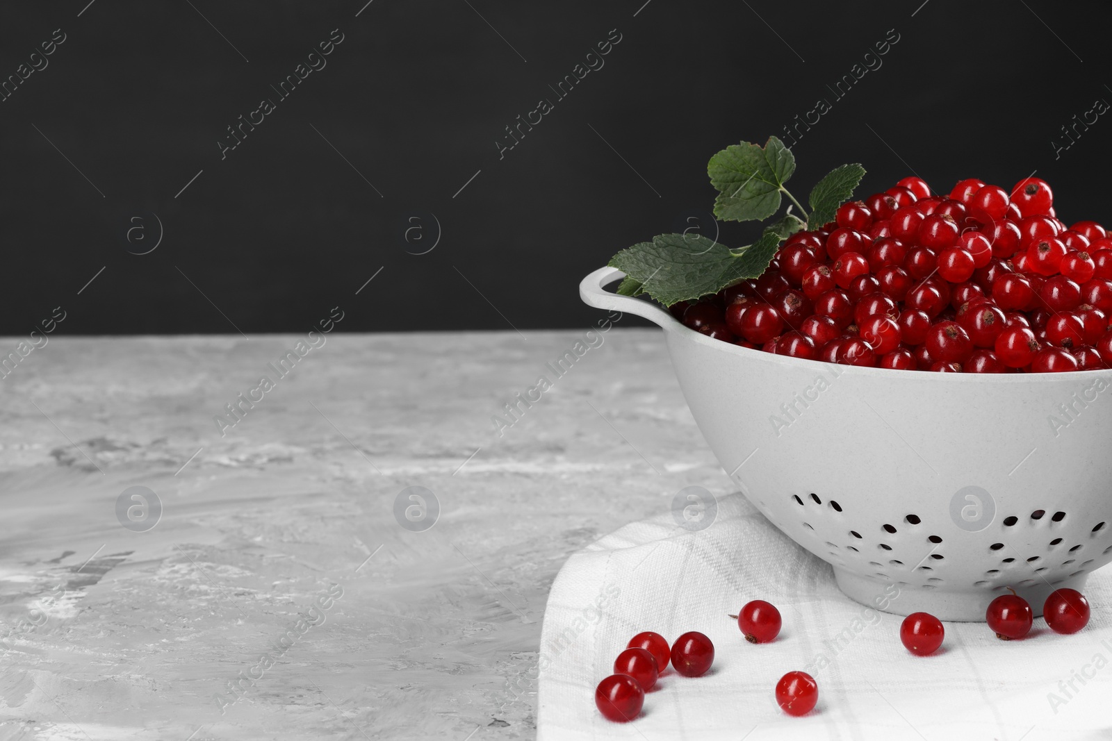 Photo of Ripe red currants and leaves in colander on grey textured table. Space for text