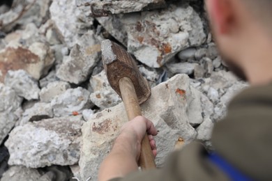 Man breaking stones with sledgehammer outdoors, closeup