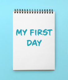 Image of New life beginning. Notebook with text My First Day on light blue background, top view