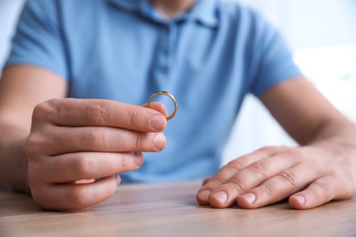 Photo of Man holding wedding ring at wooden table, closeup. Divorce concept