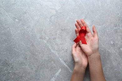 Photo of Woman holding red awareness ribbon at light grey marble table, top view with space for text. World AIDS disease day