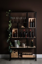 Rack with bottles of wine and glasses near brown wall