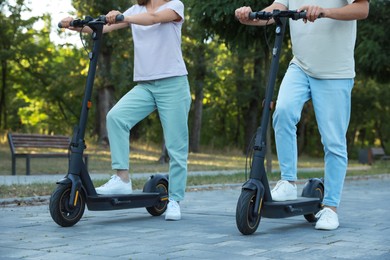 Couple riding modern electric kick scooters in park, closeup