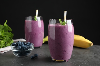 Photo of Glasses of delicious blueberry smoothie on grey table against black background