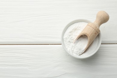 Baking powder in bowl and scoop on white wooden table, top view. Space for text