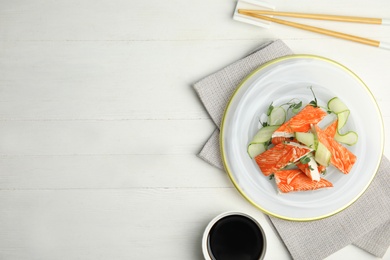 Photo of Fresh crab sticks with cucumber served on white wooden table, flat lay. Space for text