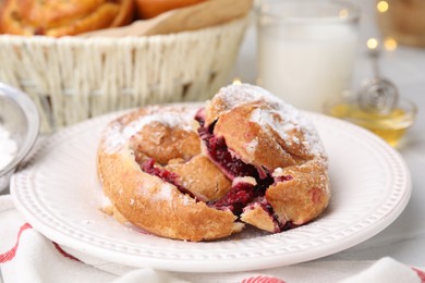 Photo of Delicious bun with sugar powder and berries on white table, closeup