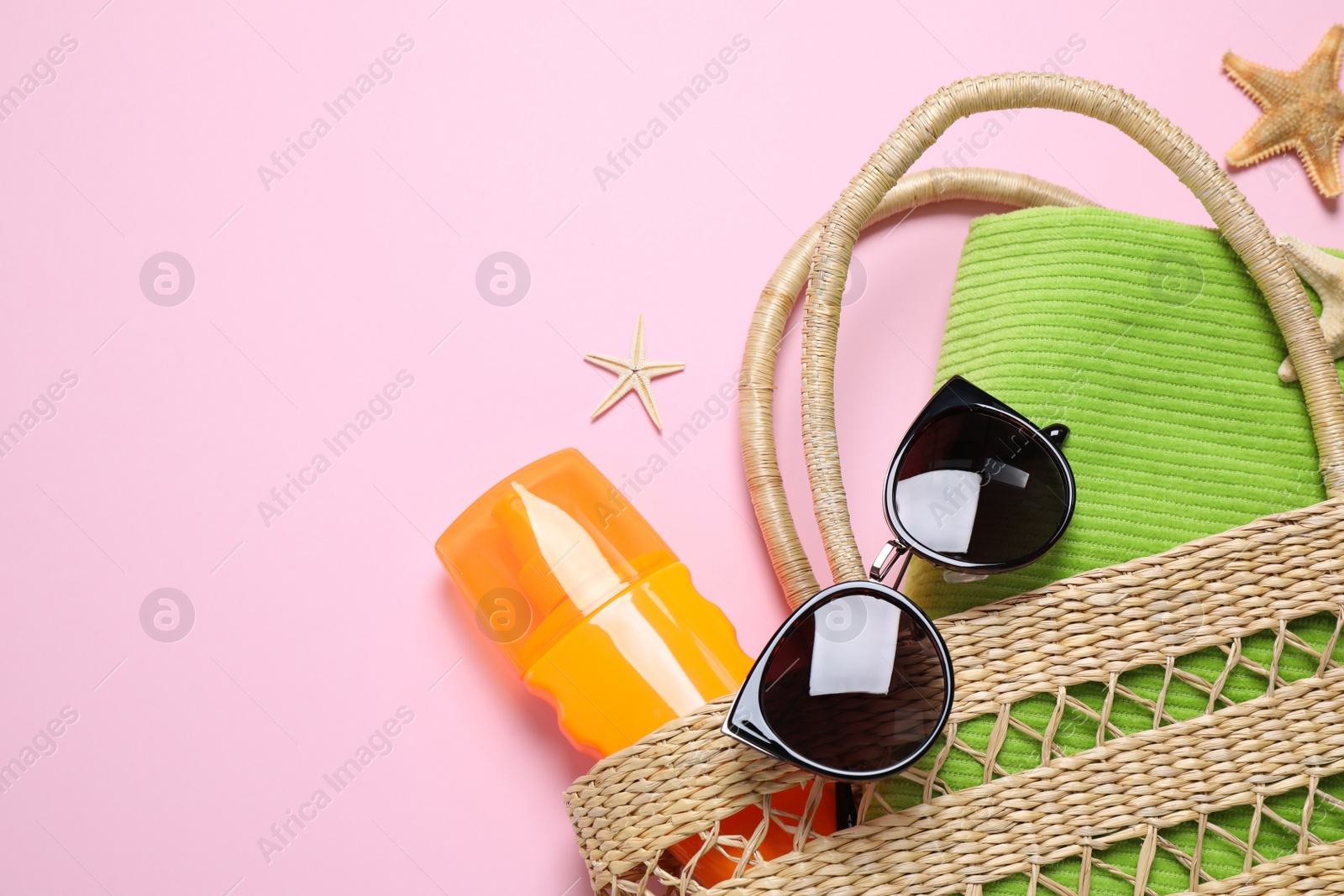 Photo of Handbag with sun protection product and beach accessories on pink background, flat lay. Space for text