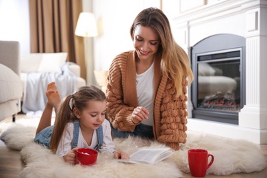 Photo of Happy woman and her daughter reading book near fireplace at home