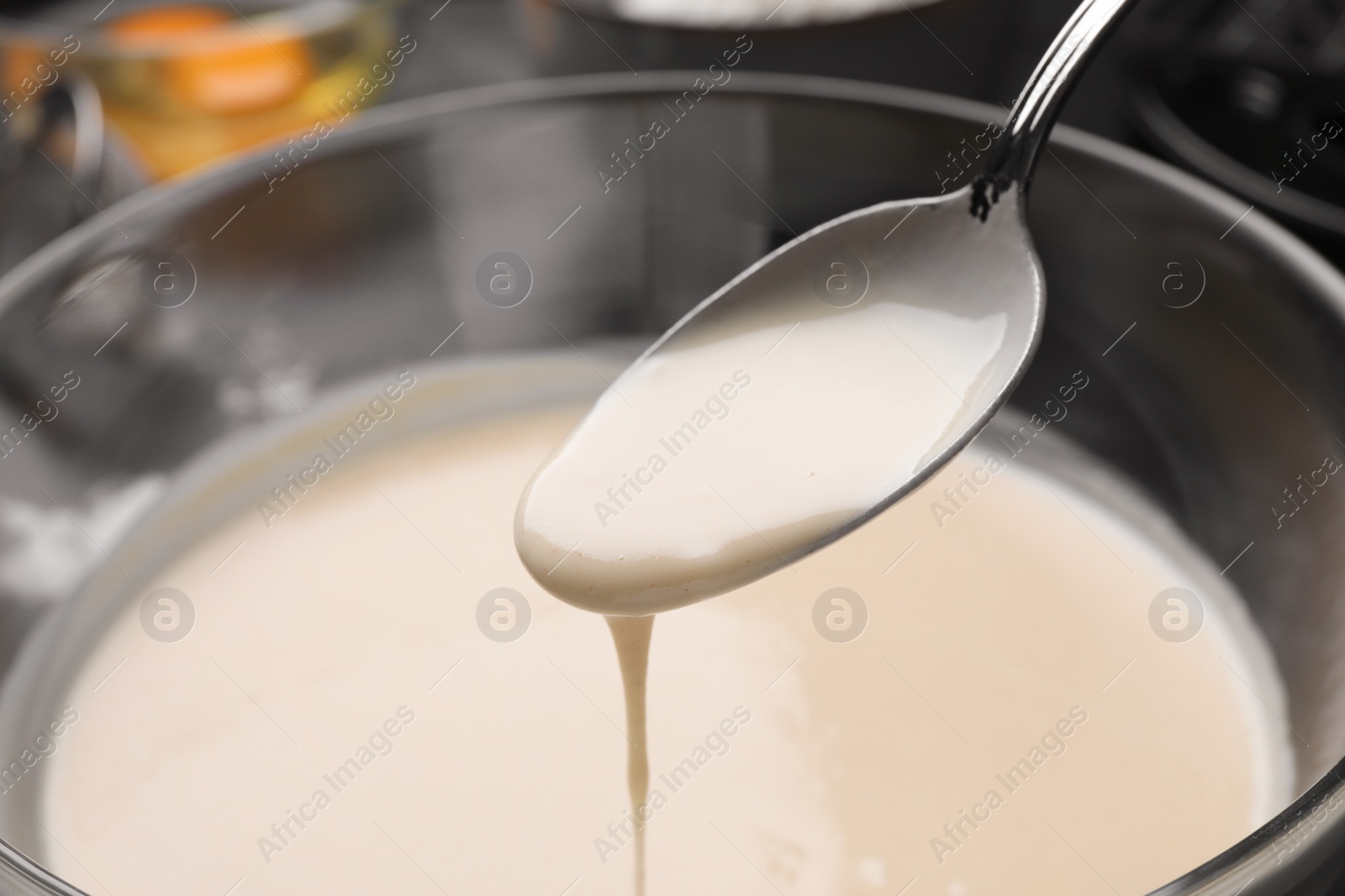 Photo of Spoon with dough for Belgian waffles over glass bowl, closeup