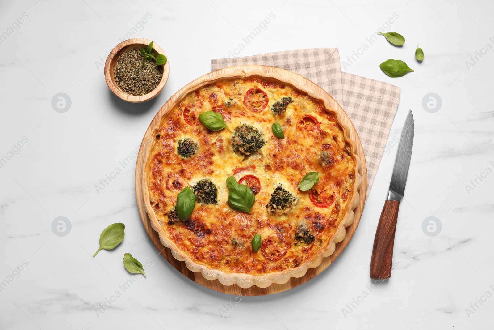 Photo of Delicious homemade vegetable quiche, basil leaves, seasoning and knife on white marble table, flat lay