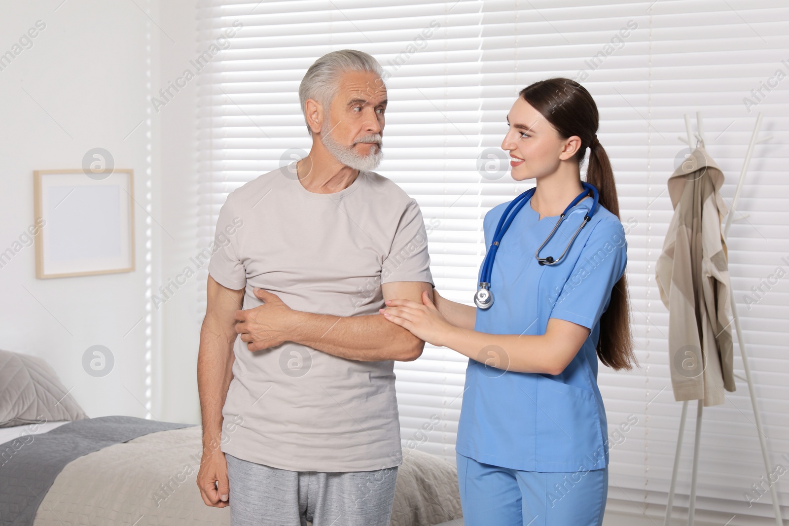 Photo of Young healthcare worker assisting senior man indoors