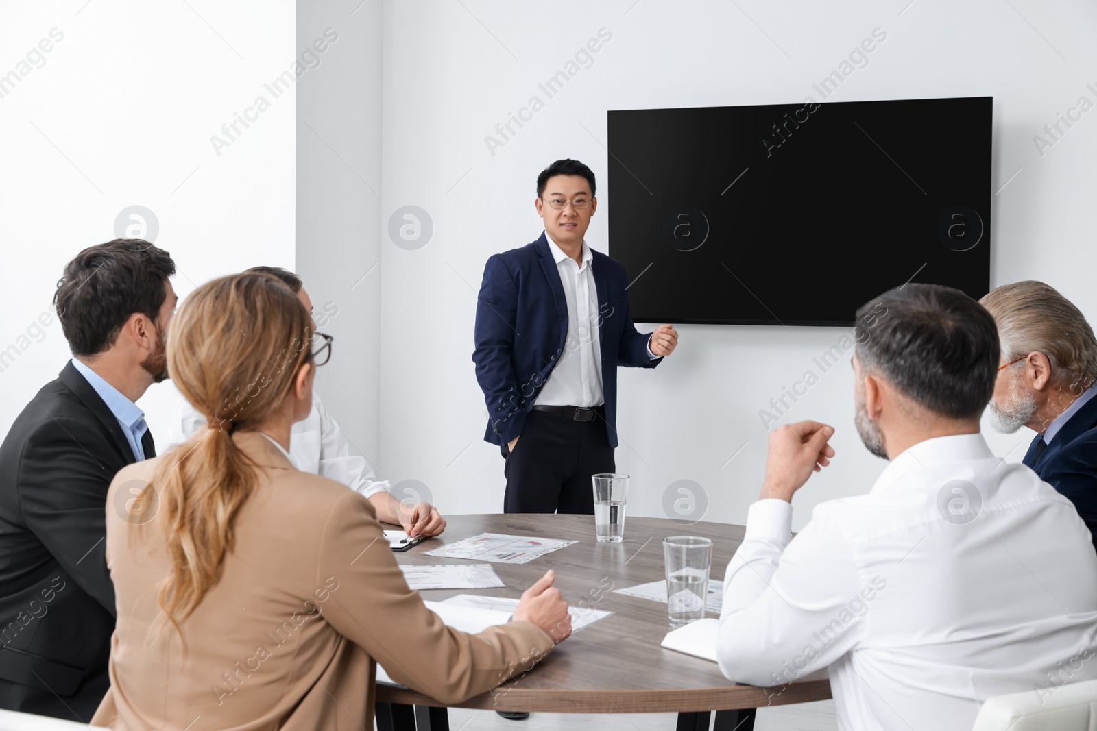 Photo of Business conference. Group of people listening to speaker report near tv screen in meeting room