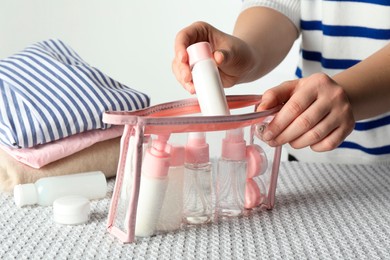 Photo of Woman putting small bottle with personal care product into plastic bag, closeup. Cosmetic travel kit