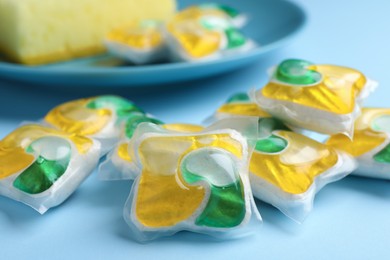 Photo of Many dishwasher detergent pods on light blue background, closeup