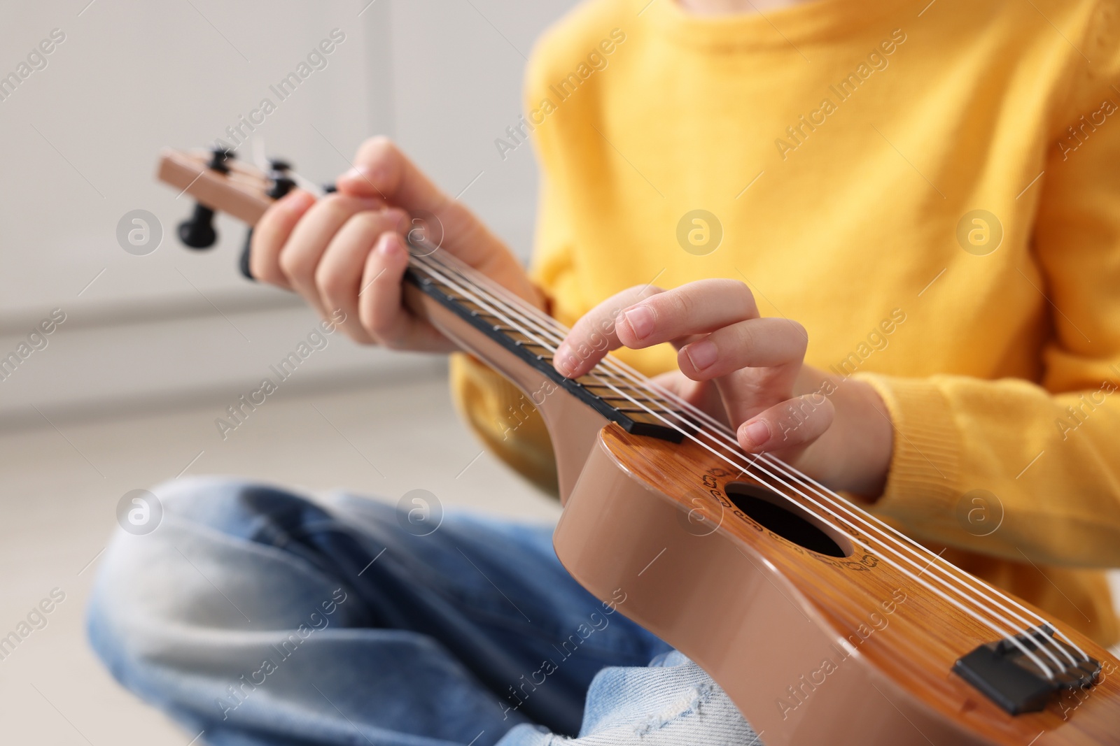 Photo of Little boy playing toy guitar indoors, closeup