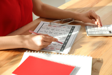 Photo of Woman marking date in calendar at wooden table, closeup