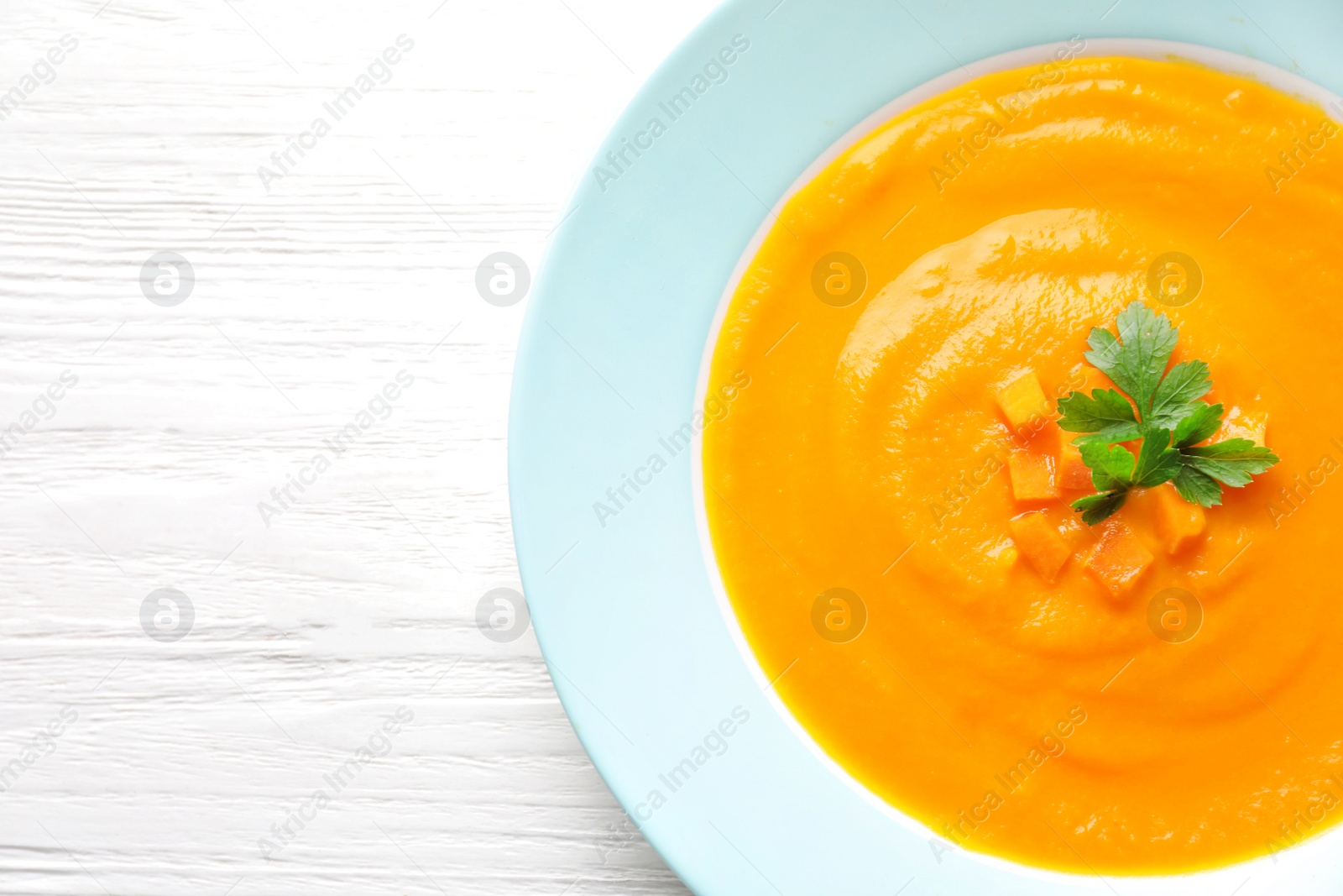 Photo of Plate of tasty pumpkin soup and space for text on wooden background, top view