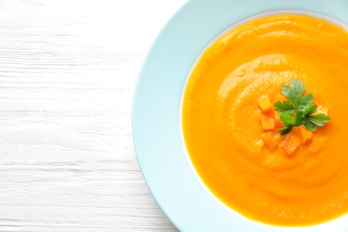 Plate of tasty pumpkin soup and space for text on wooden background, top view