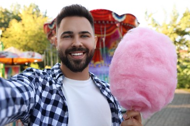 Photo of Happy young man with cotton candy taking selfie at funfair