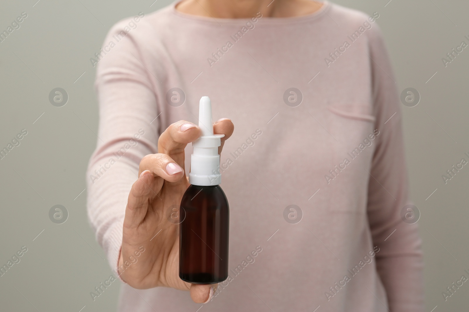 Photo of Woman holding nasal spray against light grey background, closeup