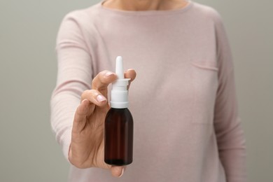 Woman holding nasal spray against light grey background, closeup