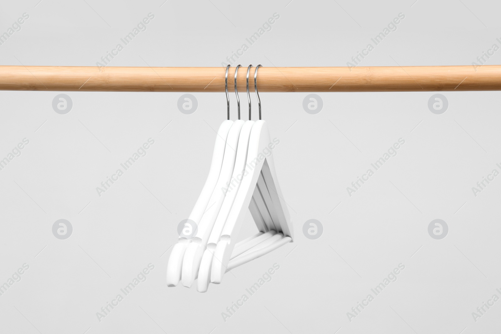 Photo of Empty clothes hangers on wooden rail against light background