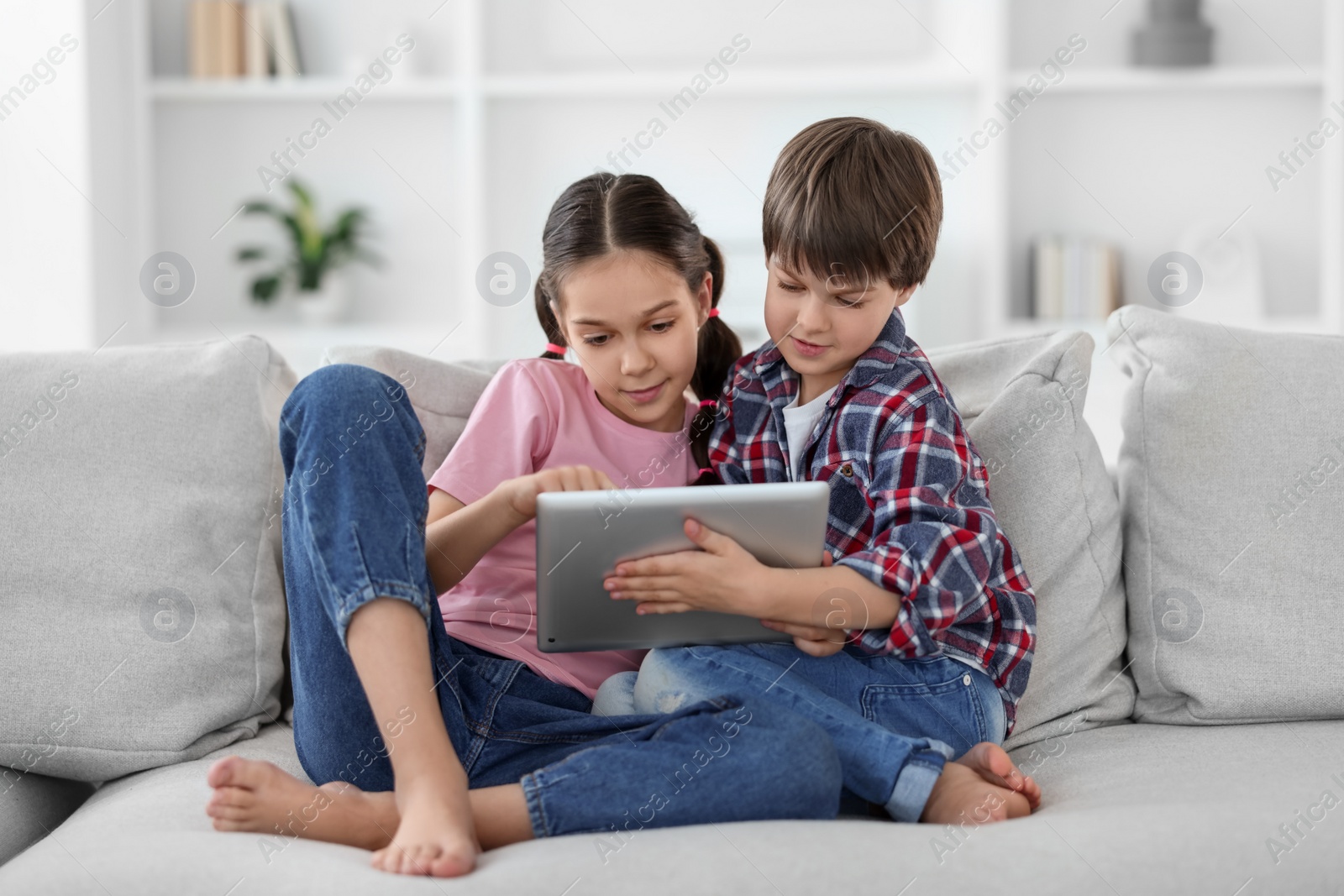 Photo of Happy brother and sister with tablet on sofa at home