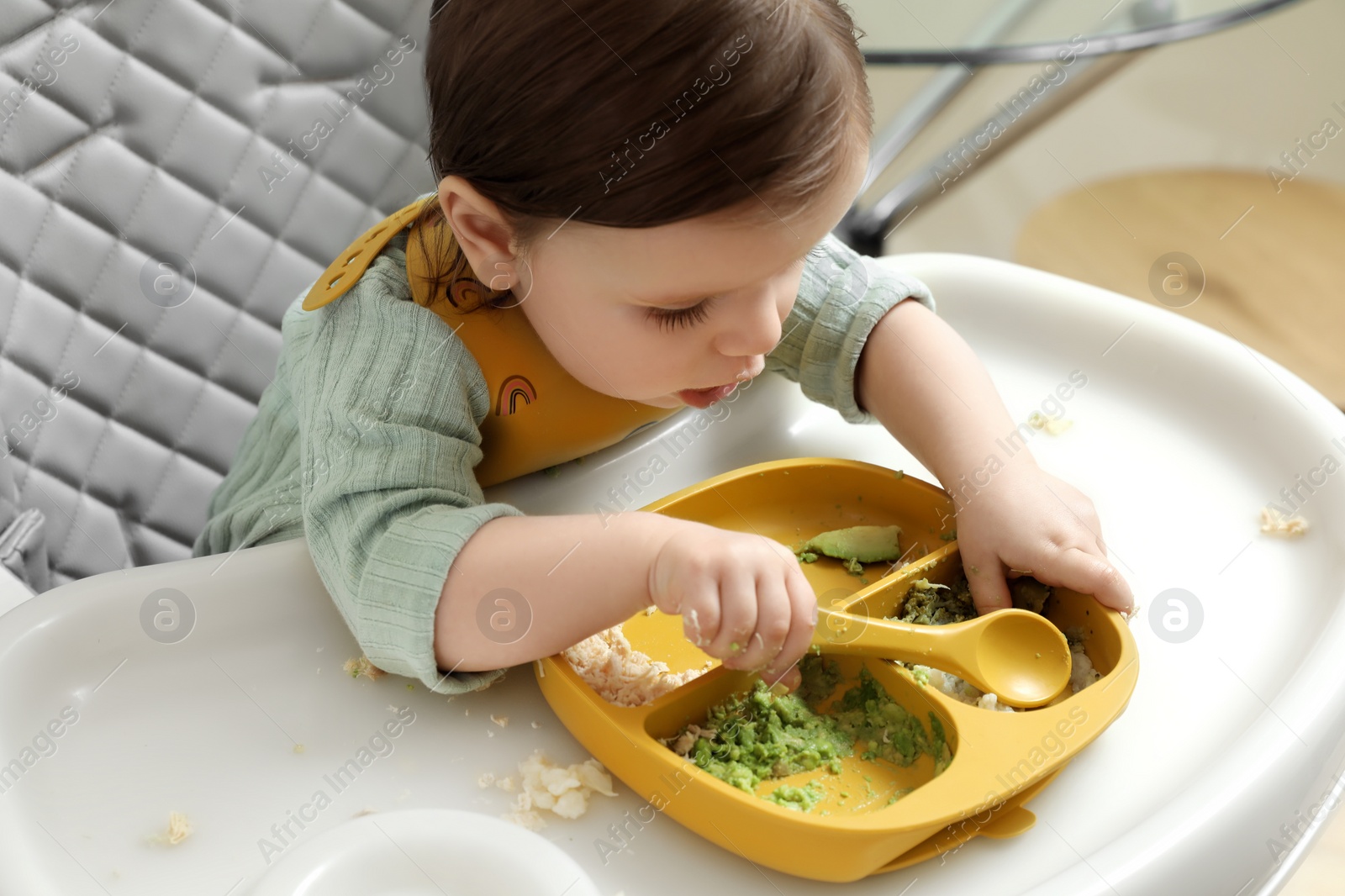 Photo of Cute little baby eating healthy food in high chair indoors