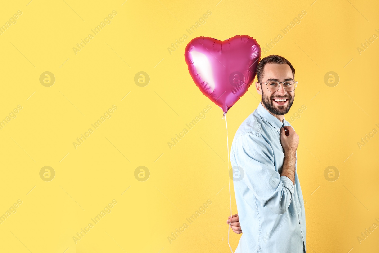 Photo of Portrait of young man with heart shaped balloon on color background. Space for text