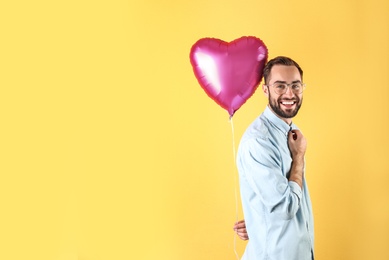 Portrait of young man with heart shaped balloon on color background. Space for text