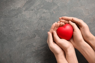 People holding red heart on gray background, top view with space for text. Cardiology concept