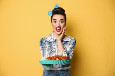 Funny young housewife with homemade pastry on color background