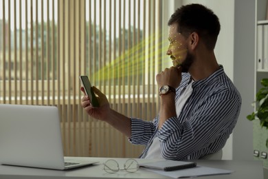 Image of Man using smartphone with facial recognition system in office. Security application scanning his face for approving owner's identity