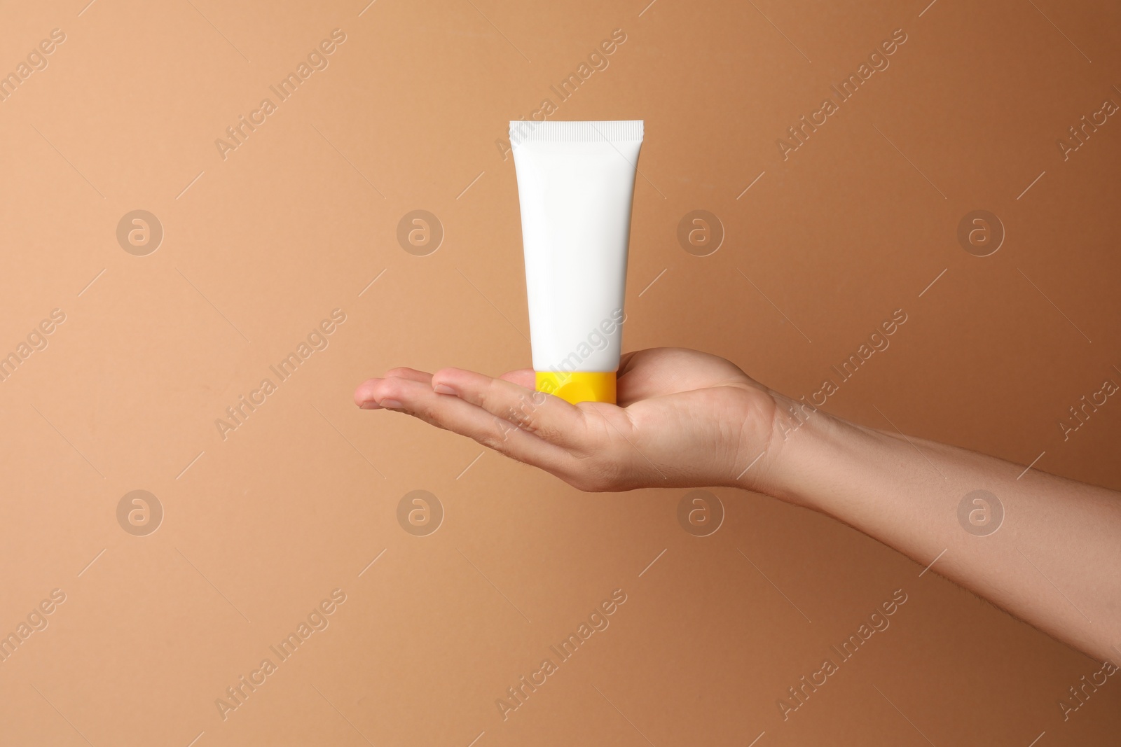 Photo of Woman holding tube of face cream on beige background, closeup. Space for text