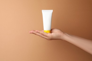 Photo of Woman holding tube of face cream on beige background, closeup. Space for text
