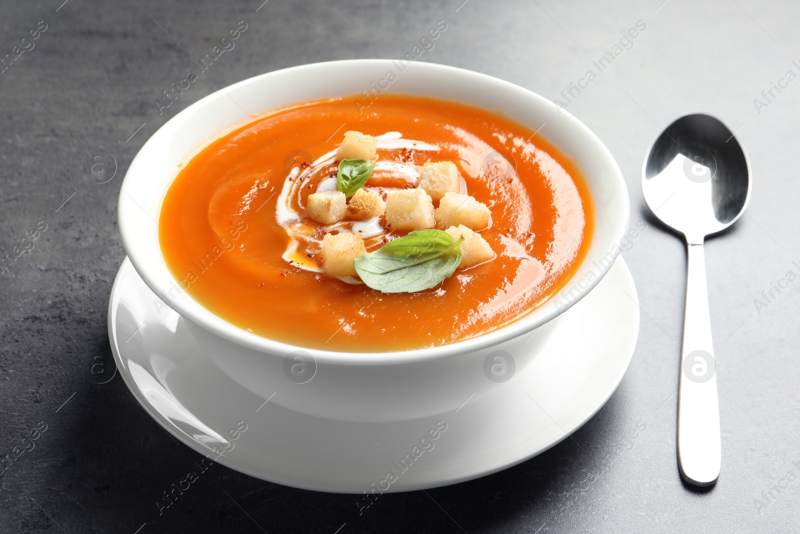 Photo of Bowl of tasty sweet potato soup and spoon on table