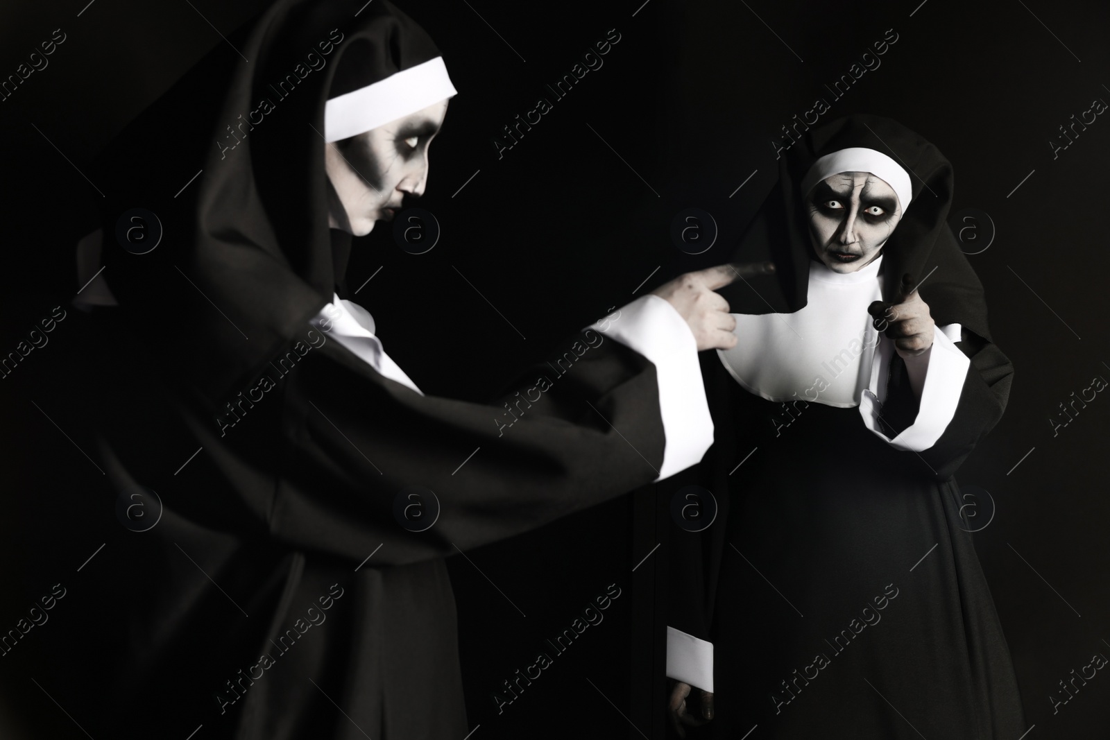 Photo of Scary devilish nun near mirror on black background. Halloween party look