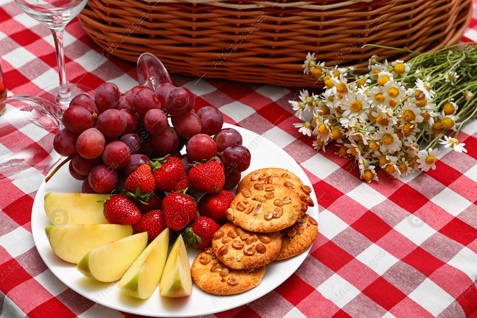 Photo of Plate with fruits and cookies near picnic basket on checkered blanket. Space for text