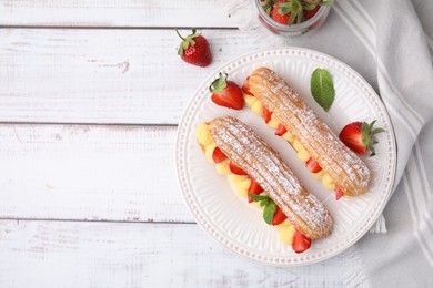 Photo of Delicious eclairs filled with cream, strawberries and mint on white wooden table, top view. Space for text