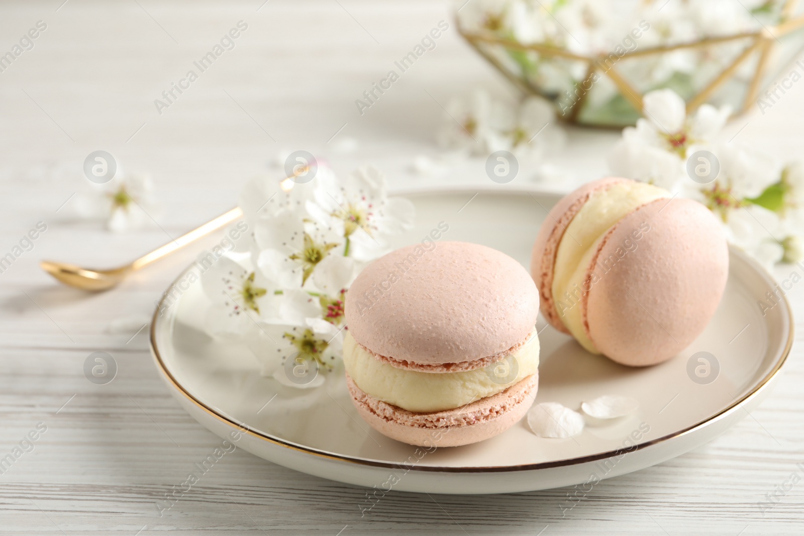 Photo of Delicious pink macarons and flowers on white wooden table