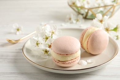 Delicious pink macarons and flowers on white wooden table