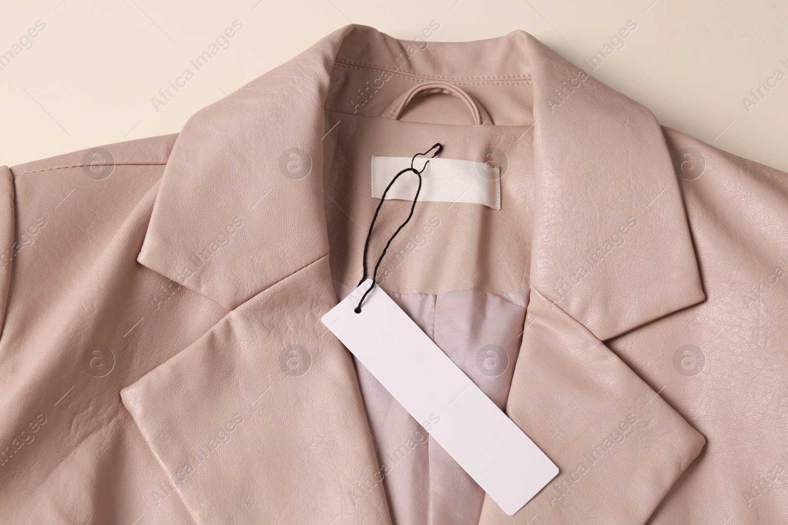 Photo of Blank white tag on beige leather jacket, top view. Space for text