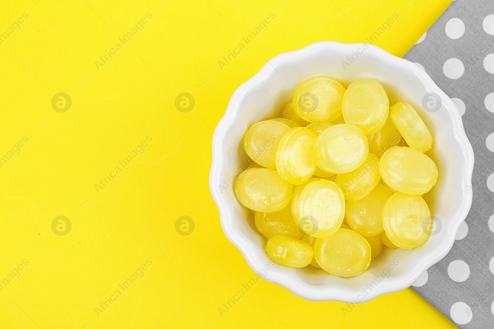 Photo of Delicious lemon drops in bowl on yellow background, flat lay. Space for text