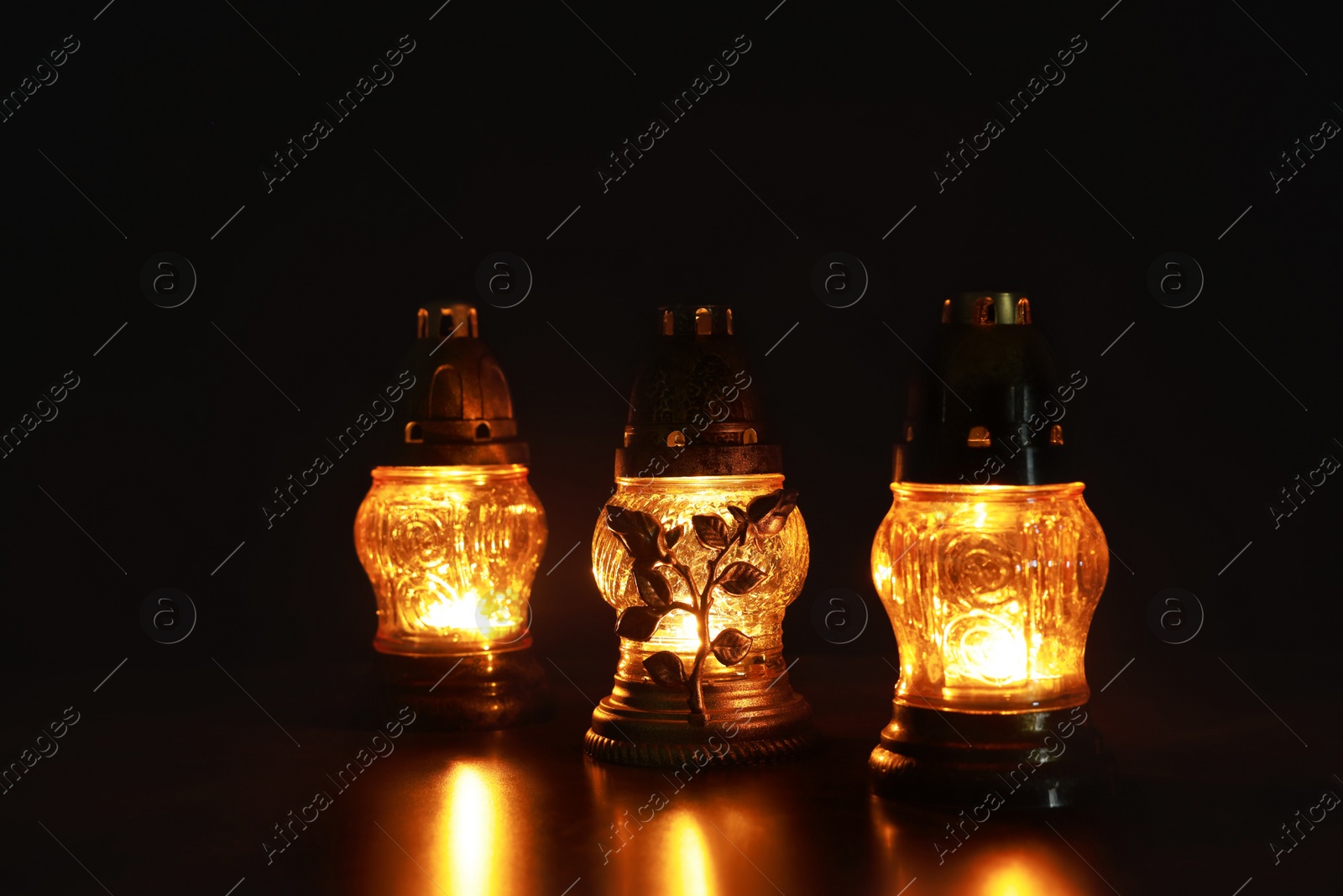 Photo of Beautiful glowing grave lights on table in darkness. Symbol of remembrance